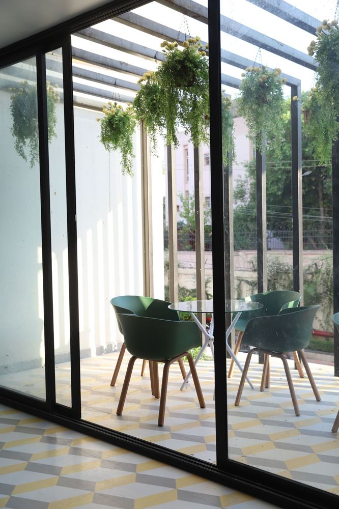 Glass-walled nook with green chairs and hanging planters